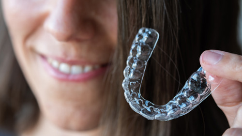 Smiling woman holding a clear dental aligner tray in Bayswater Halloween guide